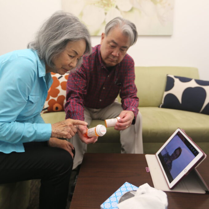 two older adults looking at pill bottles with doctor on iPad